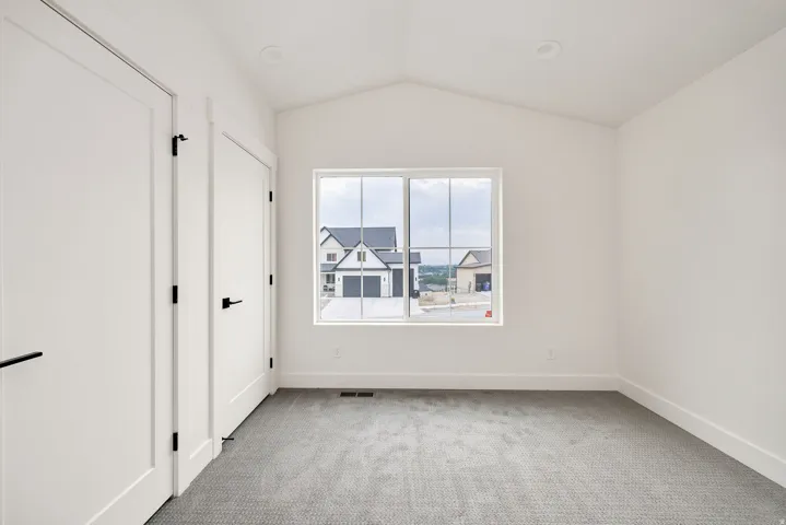 Vaulted ceiling with recessed lighting, large window, two interior doors with matte black hardware, and gray textured carpet