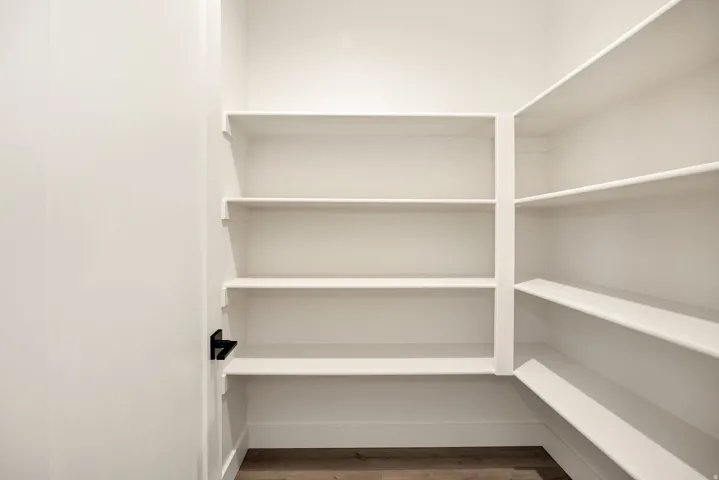 Spacious pantry featuring extensive built-in shelving, white finish, wood-finish flooring, and a black door handle