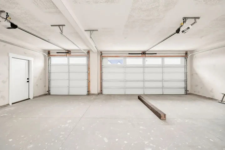 Two-car garage featuring a concrete floor, two automatic garage door openers, and a side entry door with black hardware