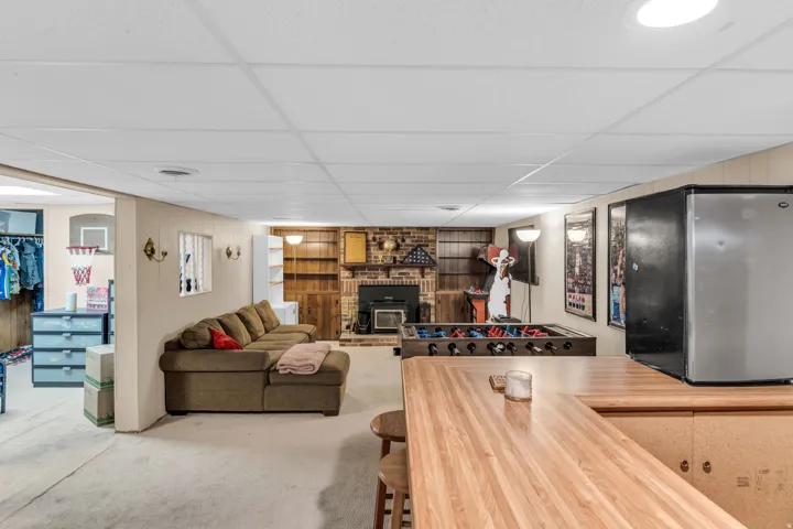 Lower level recreation room featuring a brick fireplace with wood-finish built-in shelving, drop ceiling with recessed lighting, and a wood-finish bar area