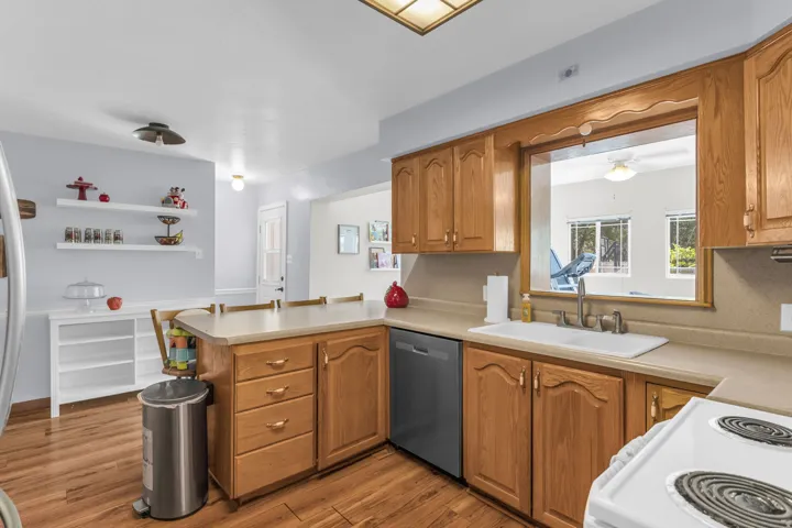 Kitchen featuring wood-finish flooring, light wood cabinetry, a double basin sink, and a pass-through window