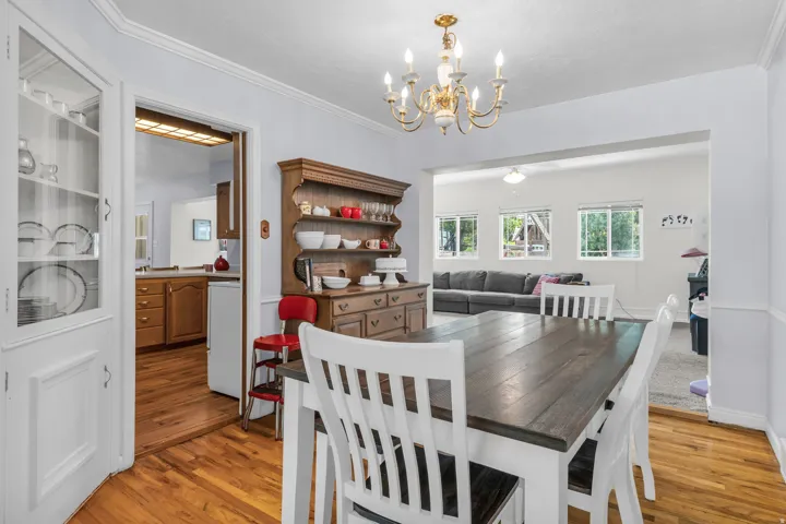 Dining area featuring wood-finish flooring, a brass-finish chandelier, and an open doorway to another room