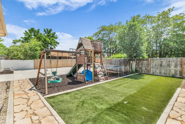 Expansive backyard featuring artificial turf, a flagstone pathway, a wood privacy fence, and a dedicated play area with a swingset and play structure