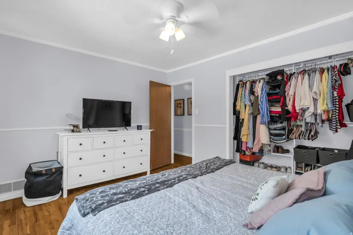 Bedroom featuring light gray walls with a white chair rail, wood-finish flooring, and white crown molding