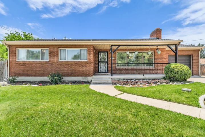 Brick exterior residence featuring a covered front porch with iron railings, a paved front walkway, and an attached garage with a dark wood-finish door