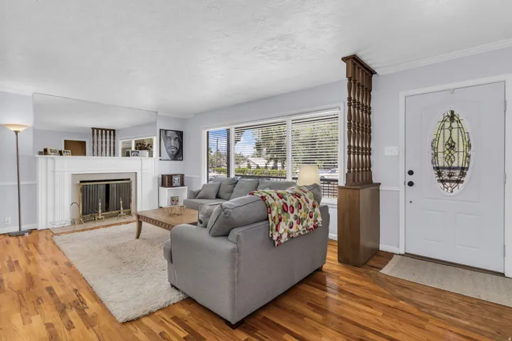 Living area featuring wood-finish flooring, a white mantel fireplace, and large windows with blinds