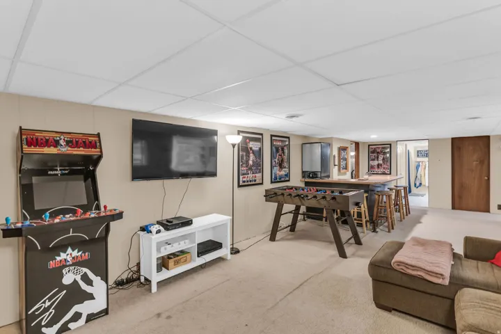 Finished lower level featuring a drop ceiling, light-toned carpeting, a built-in bar with wood-finish top and metal base, and paneled walls