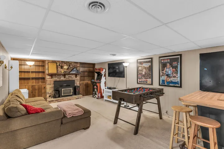 Finished lower level featuring a brick fireplace with an insert, built-in wood shelving, a drop ceiling, and carpeted flooring