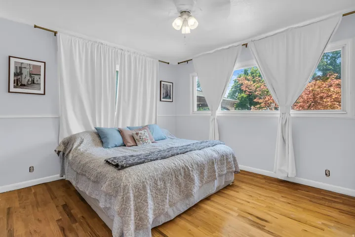 Bedroom featuring wood-finish flooring, light blue walls, and a white ceiling fan with integrated lighting