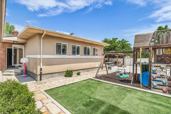 Backyard featuring artificial turf, a flagstone path, and a beige stucco exterior with multiple windows