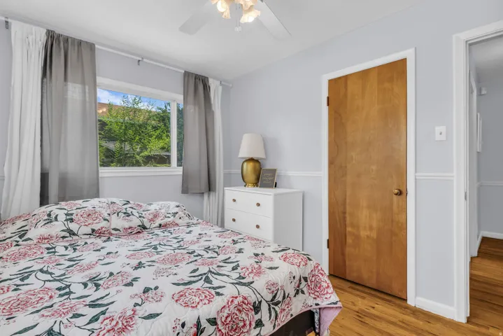 Bedroom featuring light blue walls with white wainscoting, wood-finish flooring, and a ceiling fan with light fixture