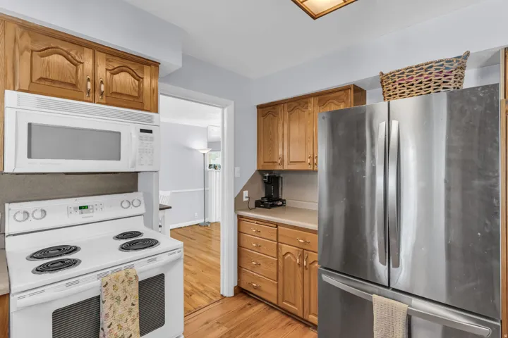 Kitchen featuring wood cabinetry, white electric range with overhead microwave, stainless steel refrigerator, and wood-finish flooring