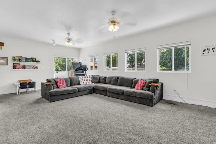 Spacious room featuring gray carpet flooring, multiple windows, a sliding glass door, and three ceiling fans