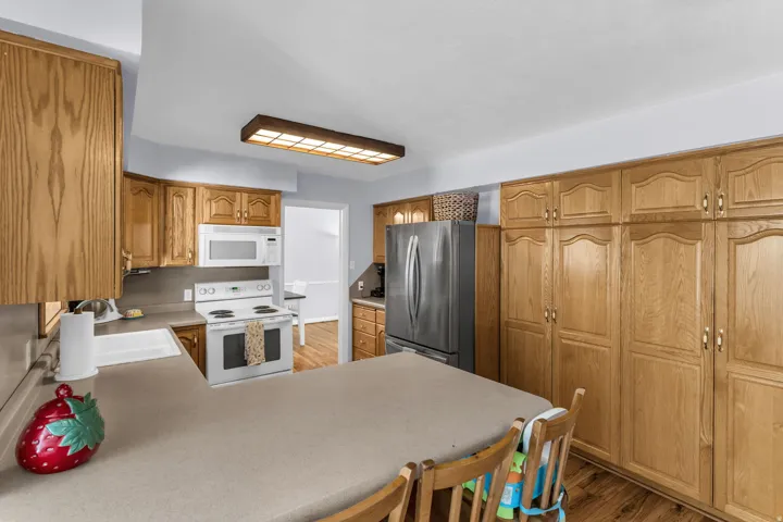Kitchen featuring extensive wood cabinetry, L-shaped countertop, white built-in appliances, and wood-finish flooring