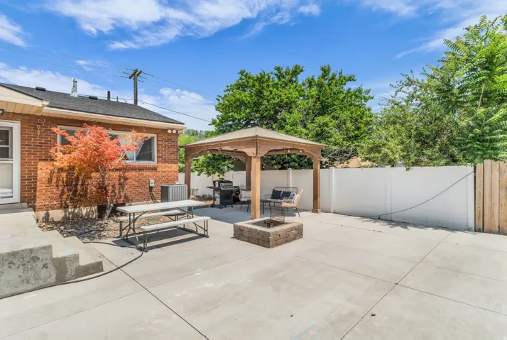 Expansive concrete patio featuring a wood gazebo, a built-in fire pit, and a privacy fence