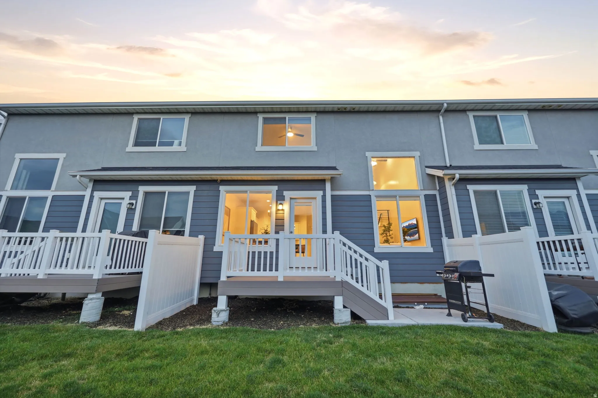 Rear exterior featuring a ground-level patio, private deck with white railing, and a vibrant green lawn