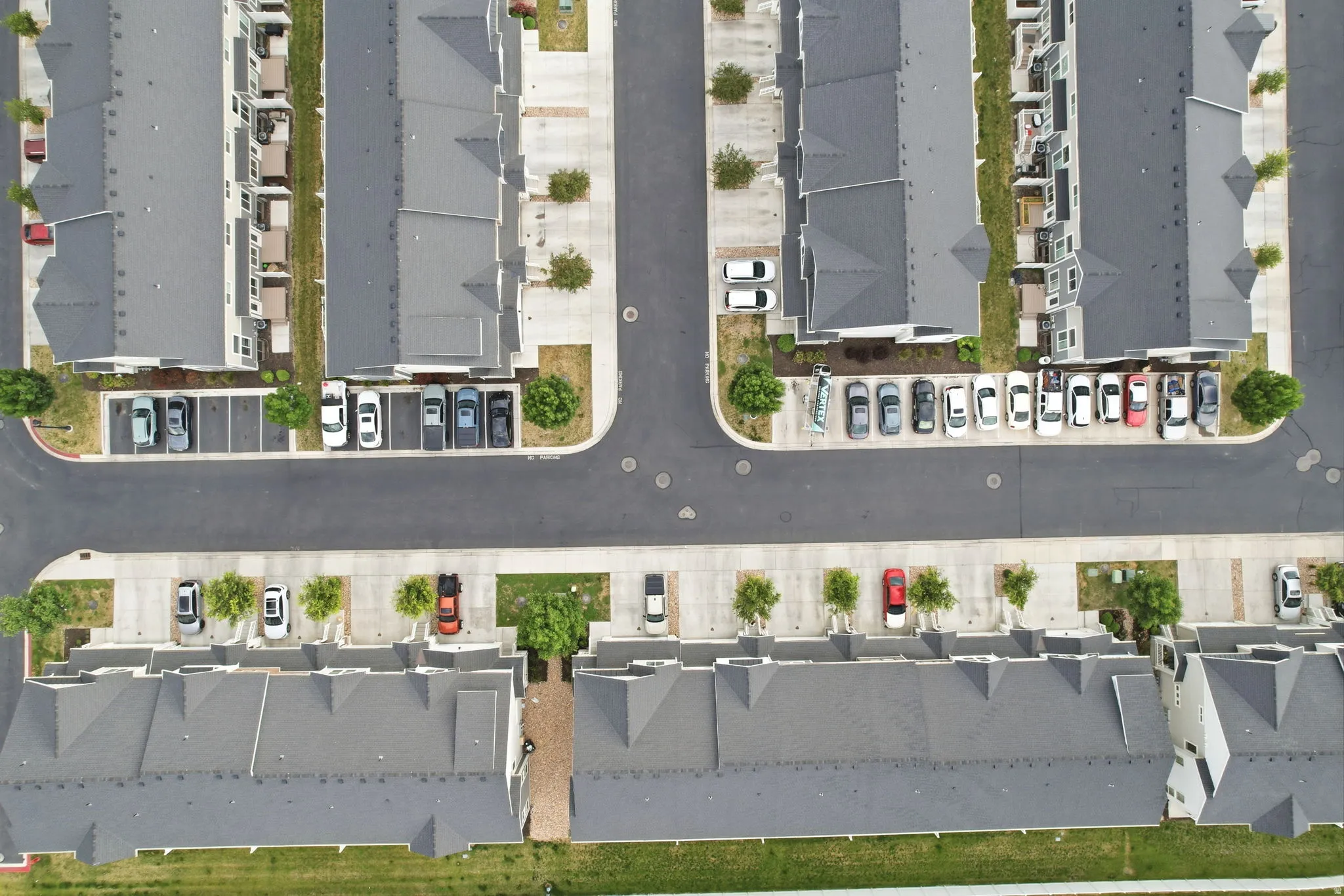 Aerial overview of a multi-unit residential complex featuring asphalt roadways, designated parking spaces, and manicured green spaces between buildings