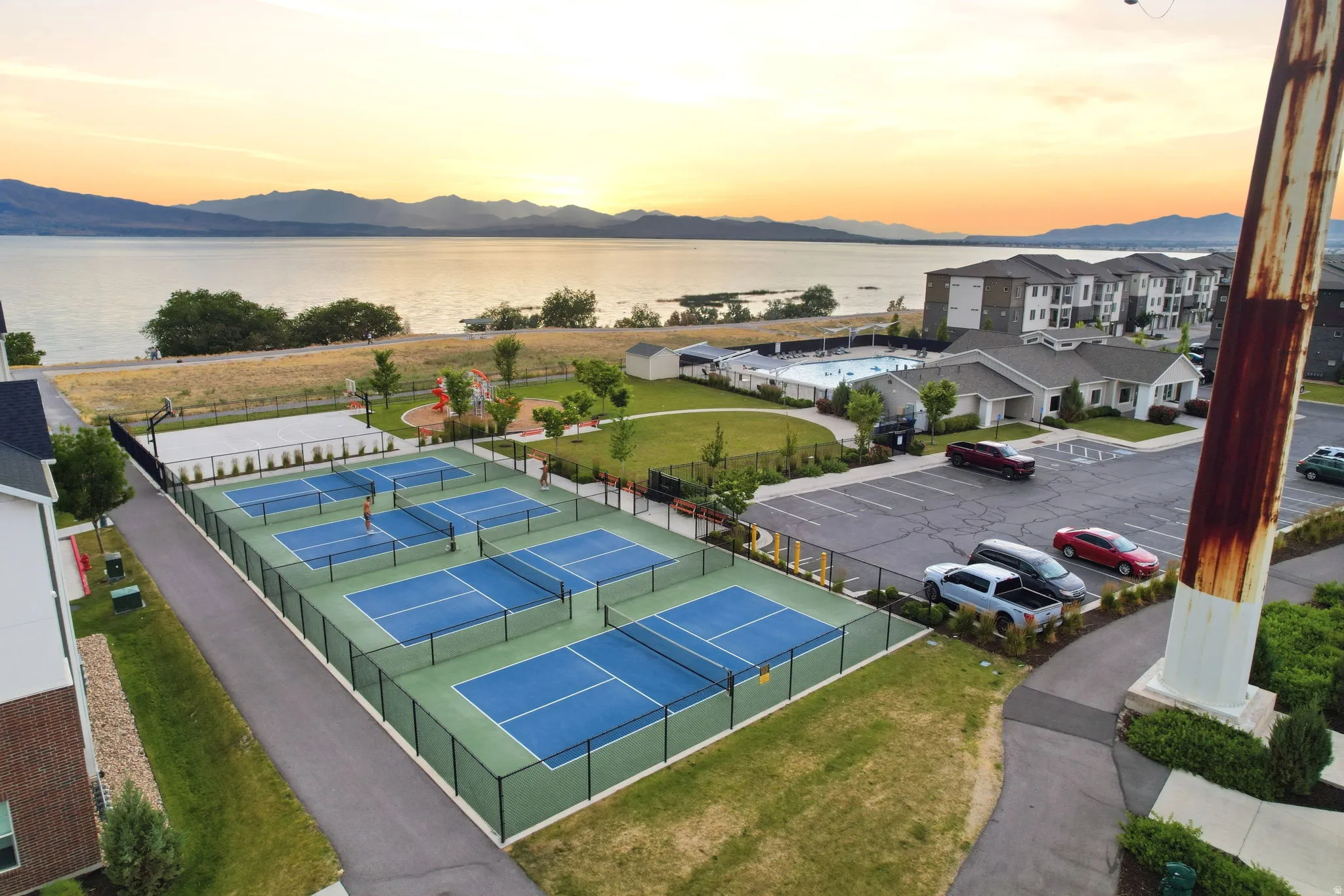 Multiple pickleball courts with perimeter fencing, a nearby swimming pool, and dedicated parking
