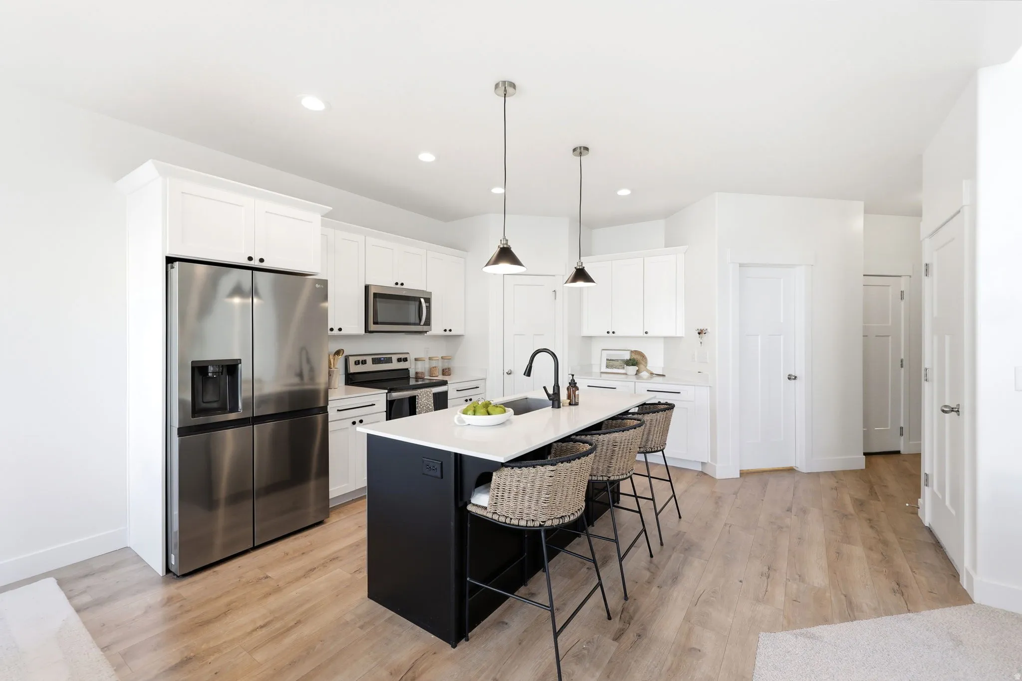 Modern kitchen featuring a white cabinetry, stainless steel appliances, a large center island with seating, pendant lighting, and wood-finish flooring