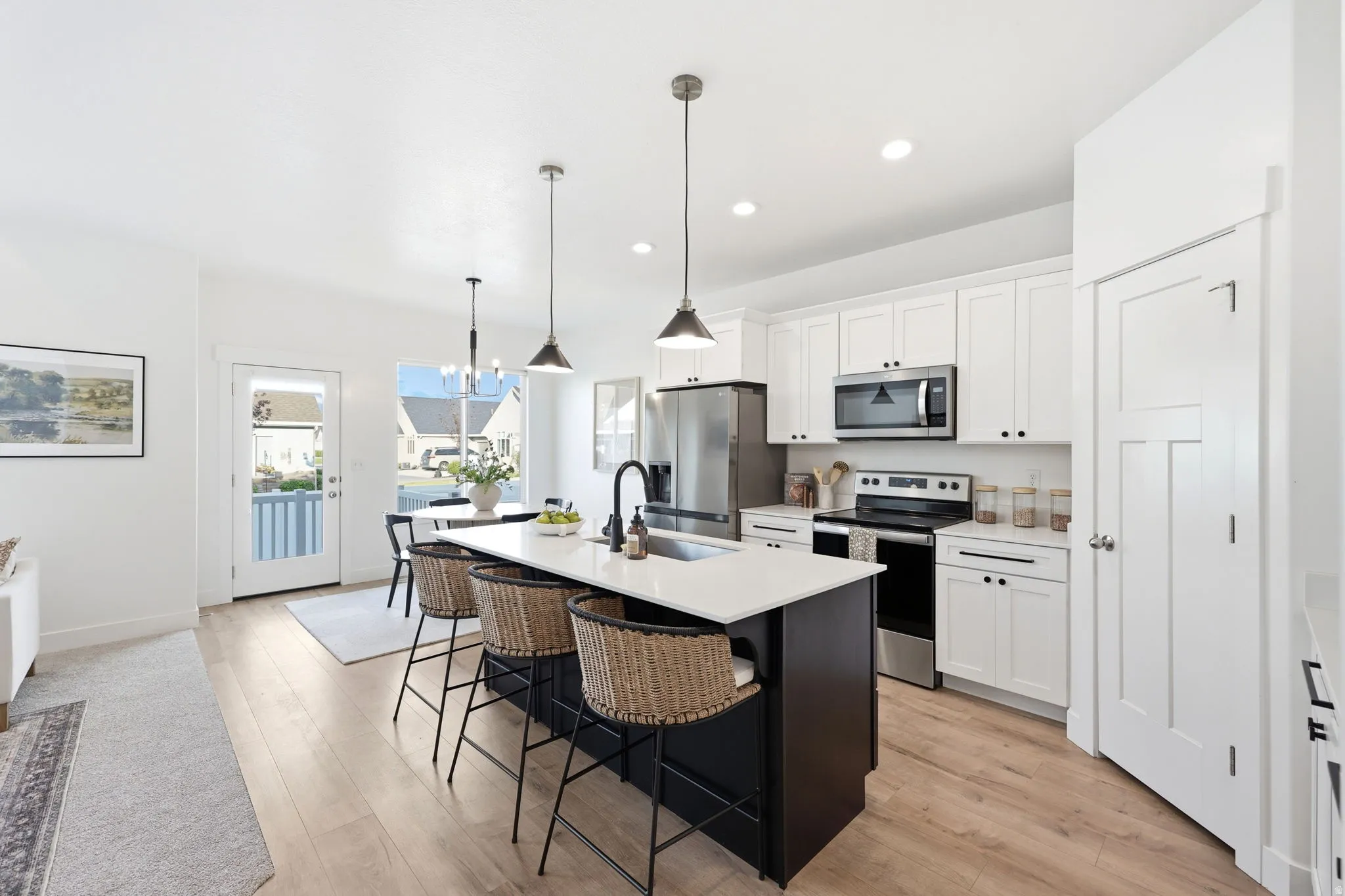 Modern kitchen featuring a central island with seating, white shaker cabinetry, stainless steel appliances, and light wood-finish flooring