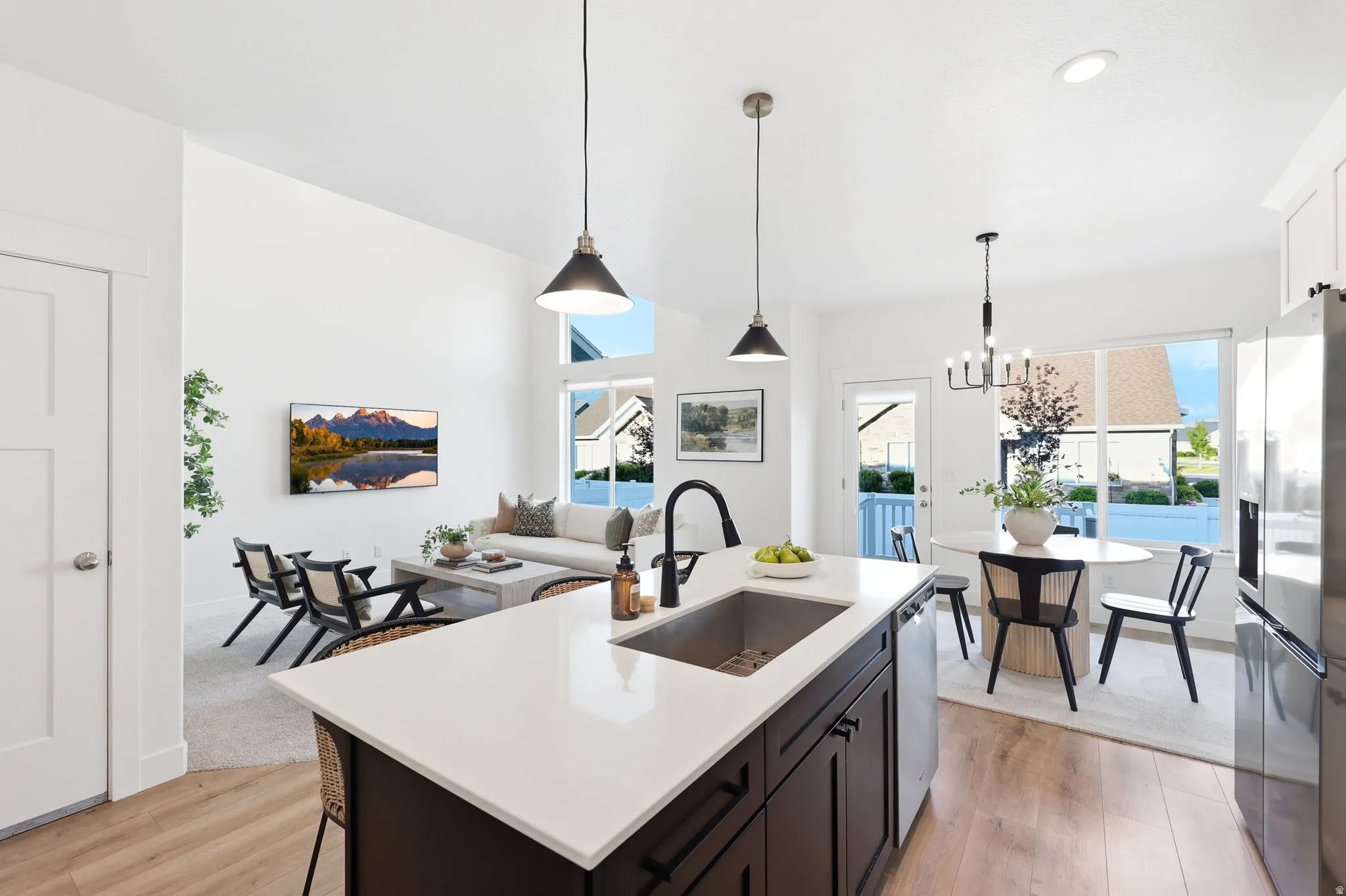 Open-concept living space with wood-finish flooring, a kitchen island featuring a deep undermount sink, and pendant lighting