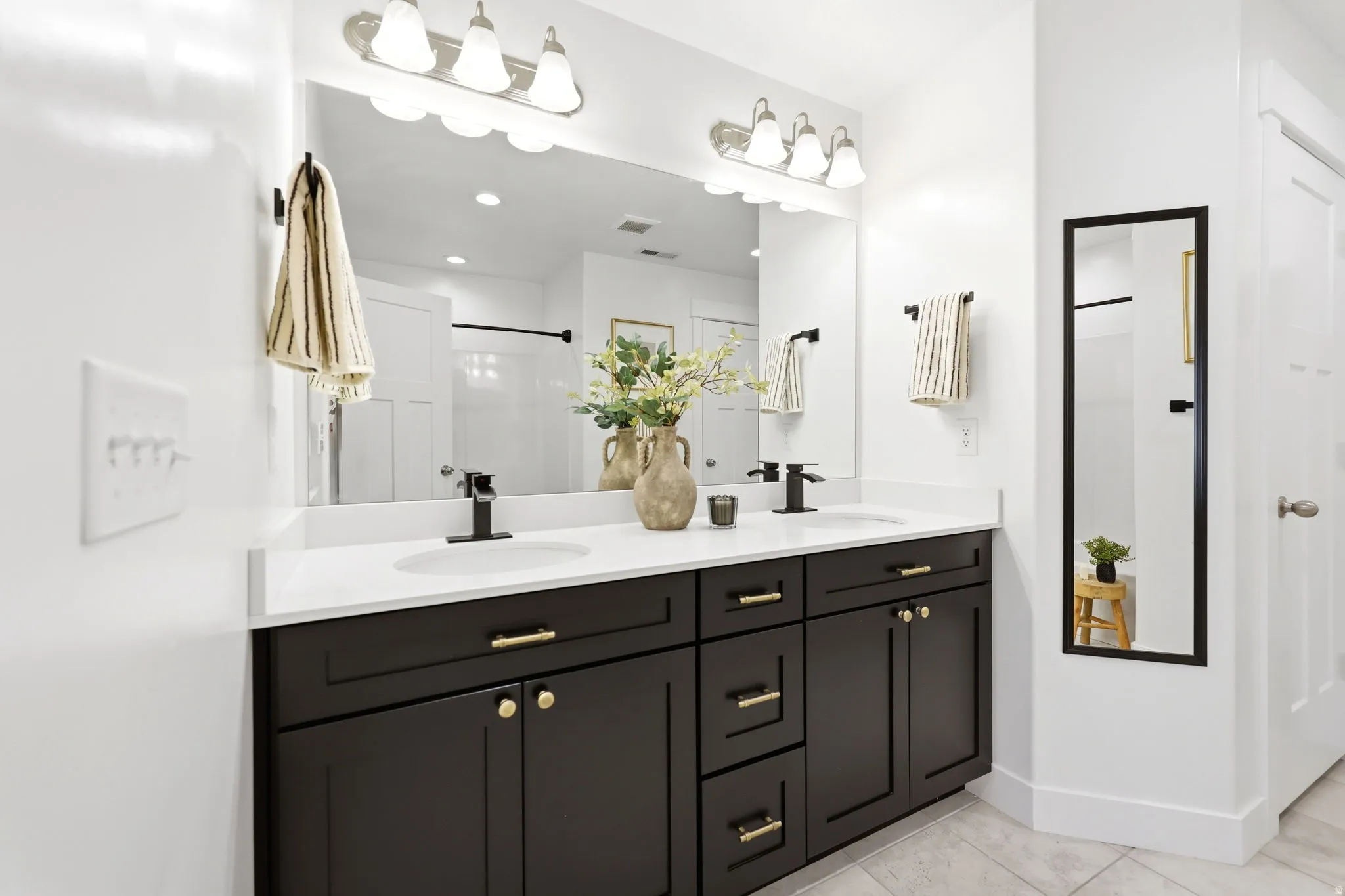 Double vanity with dark cabinetry and gold-finish hardware, individual undermount sinks, and white countertops