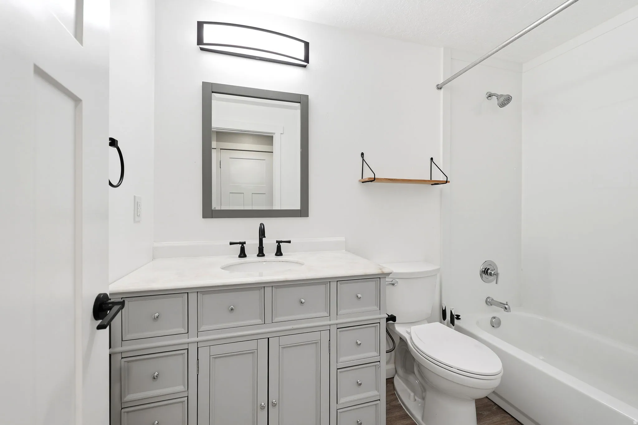 Bathroom featuring a light gray vanity with a white countertop, a rectangular framed mirror, a matte black faucet, and a white bathtub with a chrome shower fixture