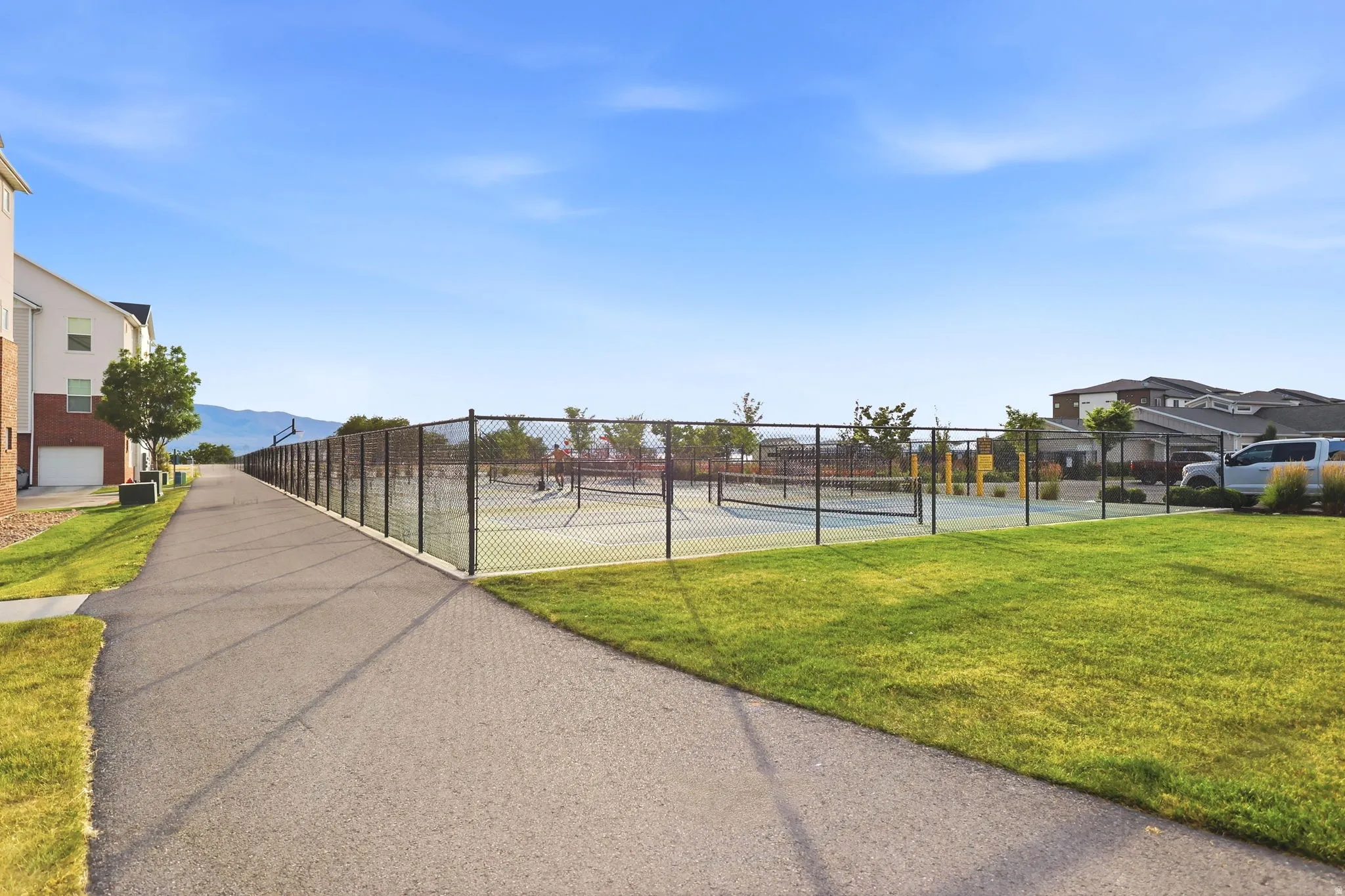 Paved pathway bordered by manicured lawn and a chain-link fence