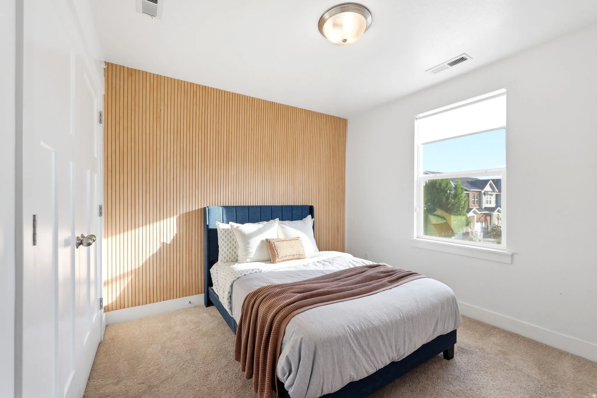 Bedroom featuring a wood-panel accent wall, neutral carpeting, and a white-framed window