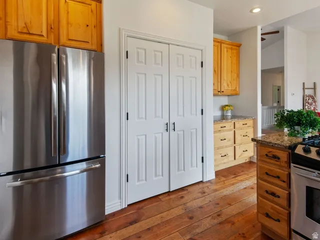 Kitchen featuring stainless steel appliances, natural wood cabinetry, wood-finish flooring, granite countertops, and white paneled pantry doors