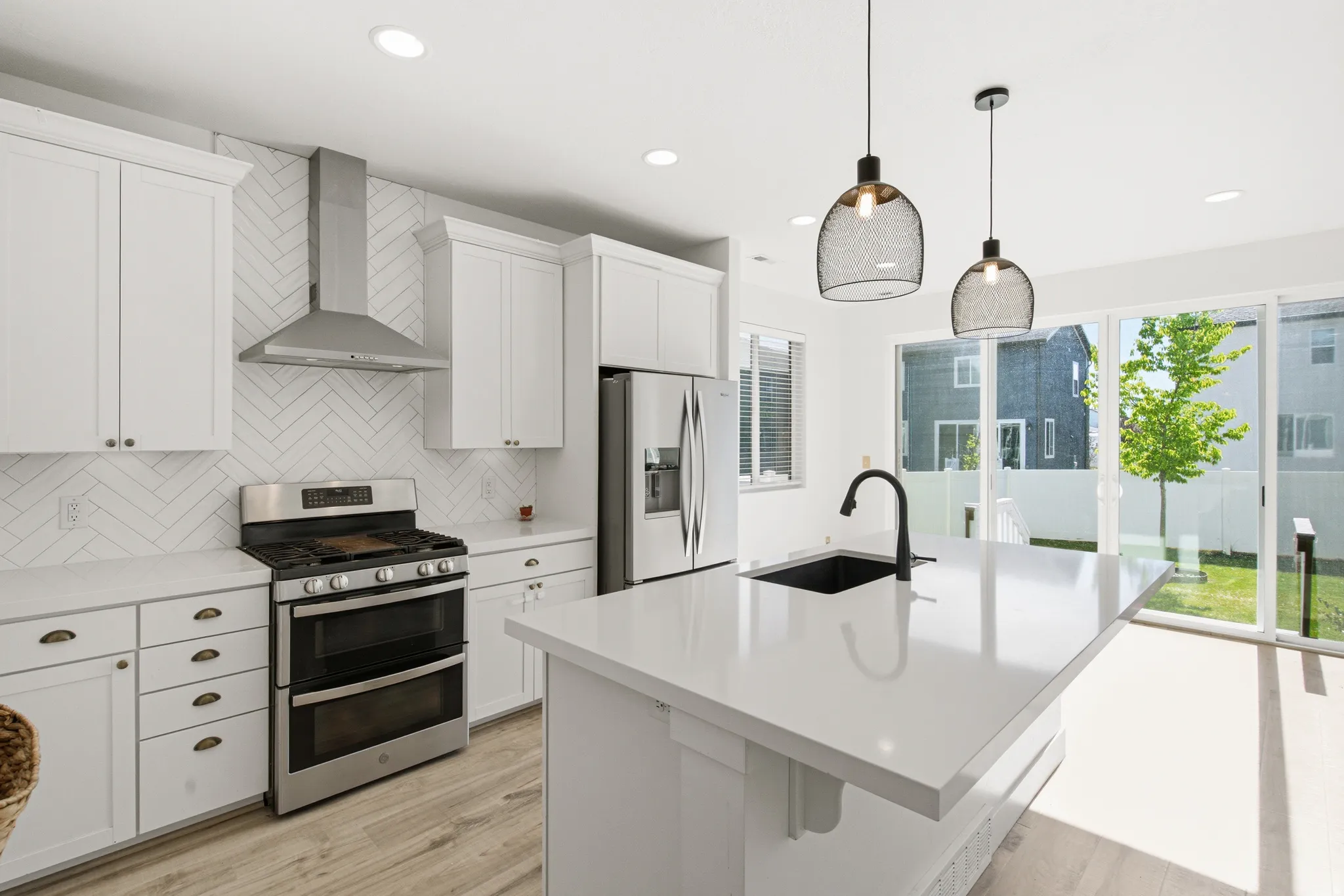 Modern kitchen featuring white cabinetry, stainless steel appliances, a herringbone tile backsplash, and a large island with an undermount sink