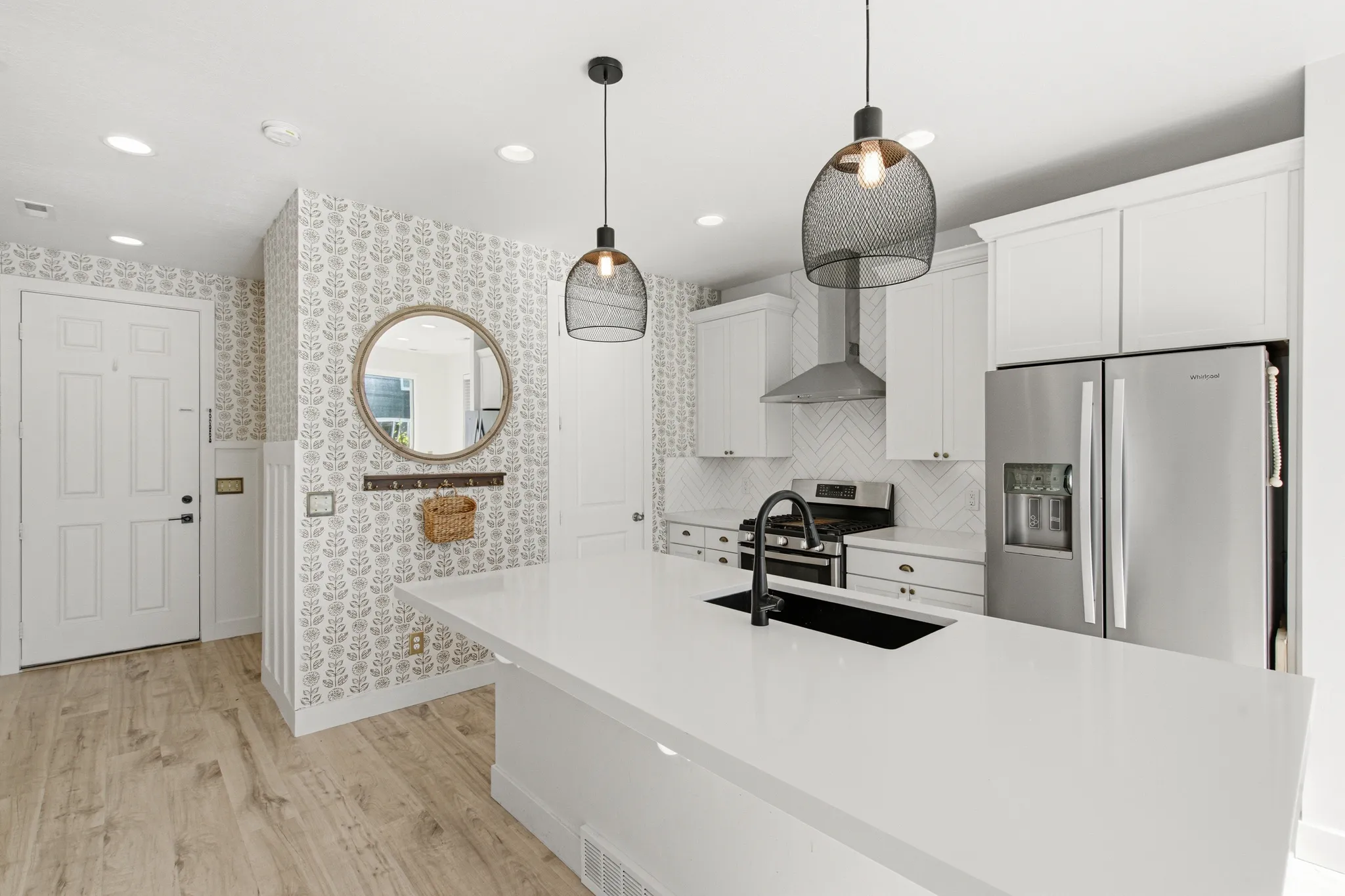 Kitchen featuring an expansive white countertop island with an undermount sink, white cabinetry, stainless steel appliances, and a chevron tile backsplash
