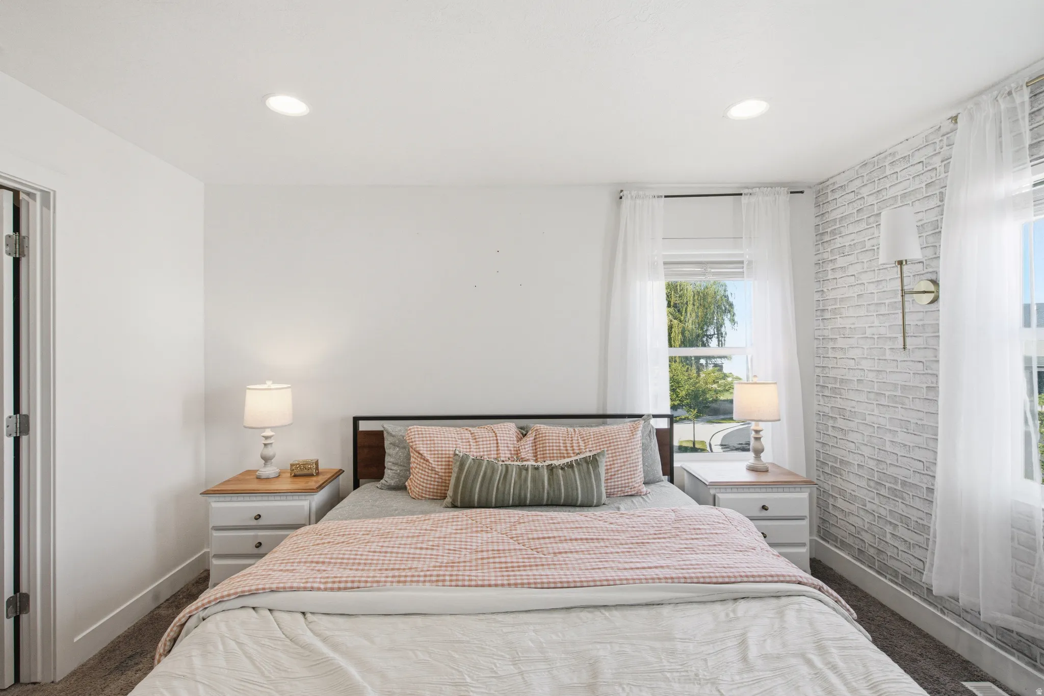 Bedroom featuring a white faux brick accent wall, two large windows, recessed lighting, and wall-mounted sconce lighting