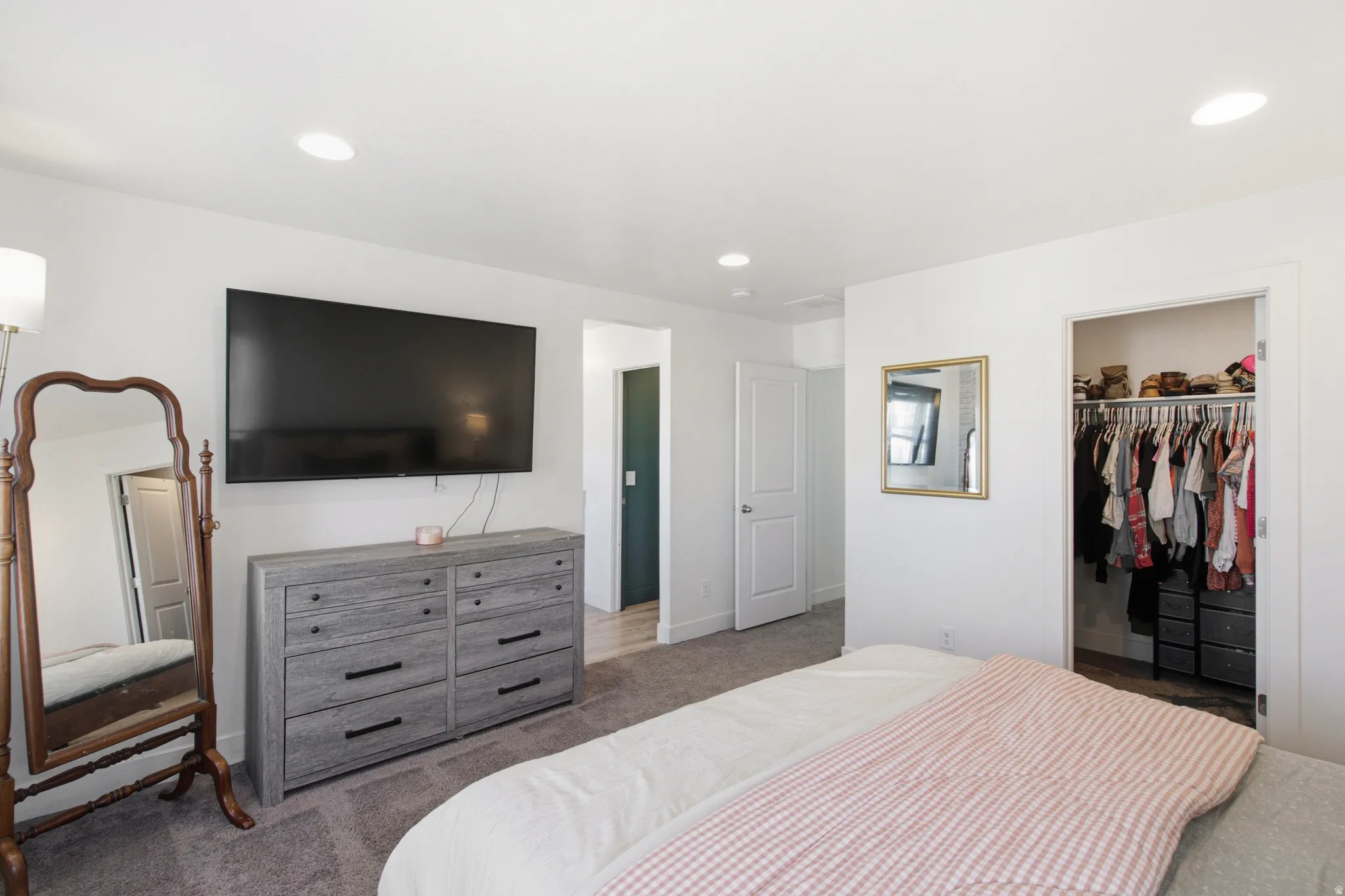 Recessed lighting illuminates this room featuring white walls, carpet flooring, and a walk-in closet with built-in shelving