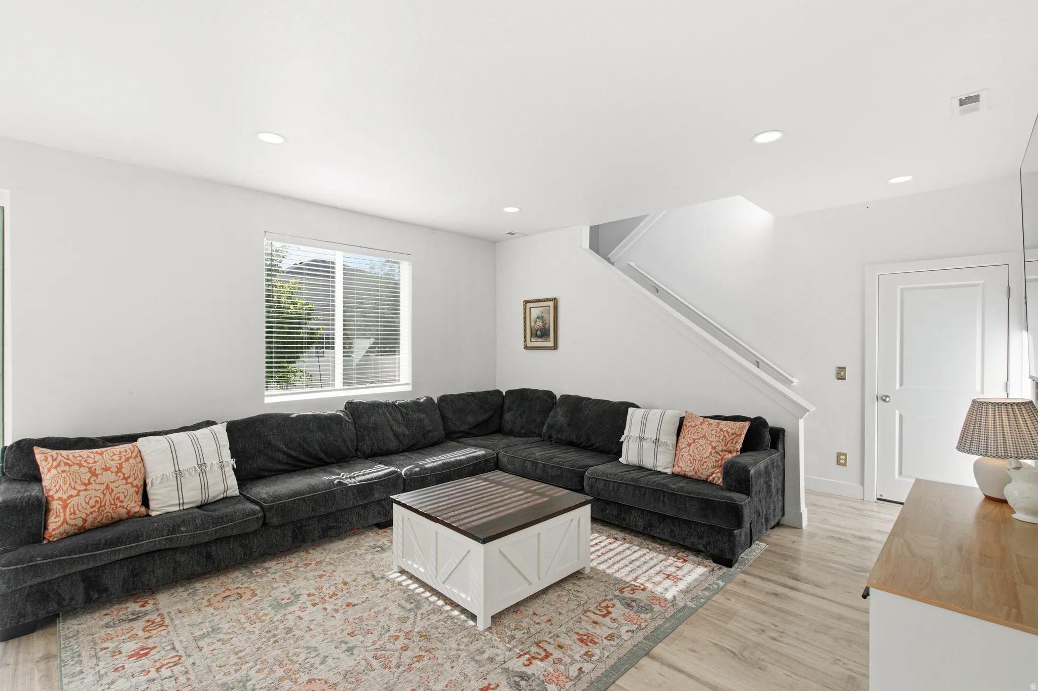 Bright living area featuring light wood-finish flooring and a staircase with white risers and railing