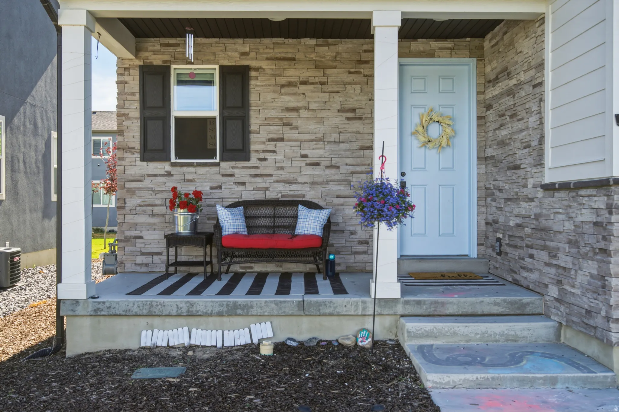 Inviting covered front porch featuring stacked stone veneer siding, a light blue entry door, white trim, and a window with dark shutters