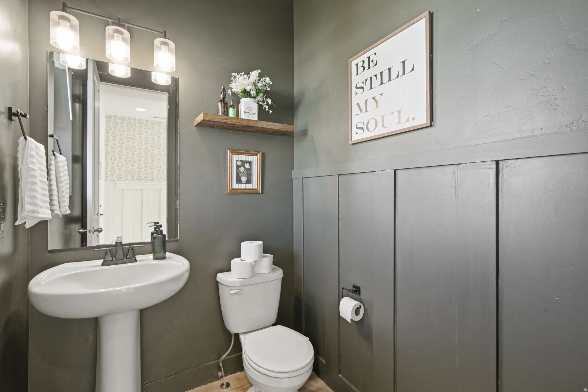 Pedestal sink with dark-toned faucet, rectangular mirror, and three-light vanity fixture