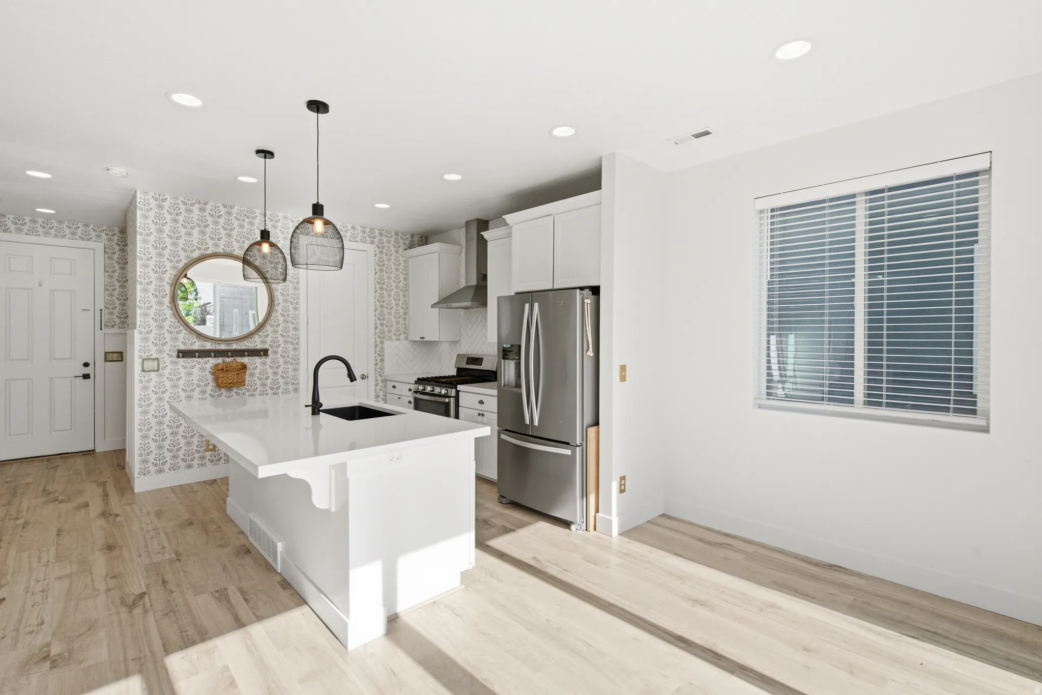 Kitchen featuring a central island with a white countertop and black sink, stainless steel appliances, white cabinetry, and wood-finish flooring