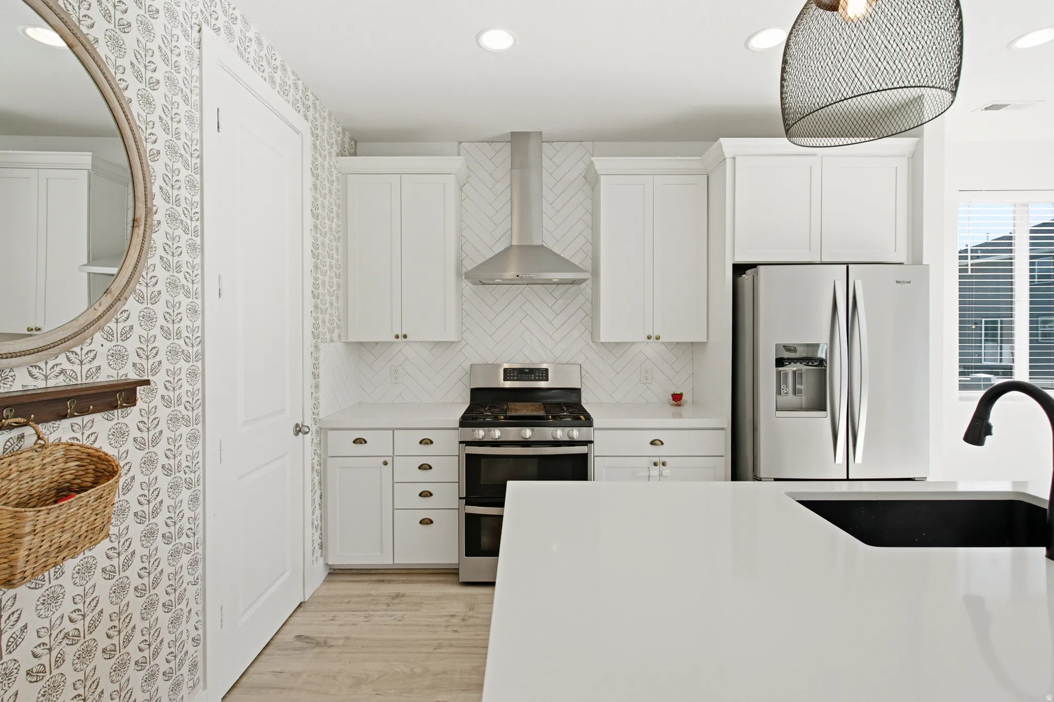 Modern kitchen featuring white cabinetry, stainless steel appliances, a white herringbone tile backsplash, light wood-finish flooring, and a large central island with a built-in sink