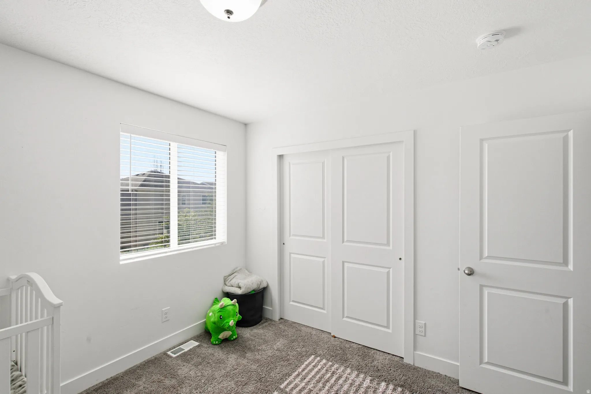 White-painted room featuring a window with horizontal blinds, a white bi-fold closet door, a white interior door with a silver knob, and a ceiling-mounted light fixture
