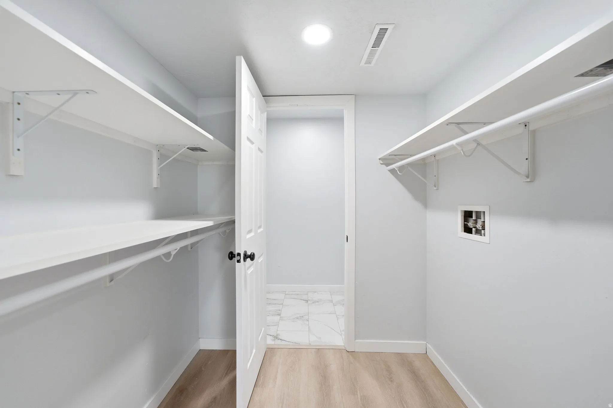 Laundry area featuring wood-finish flooring, white shelving, clothing rods, and a utility hookup