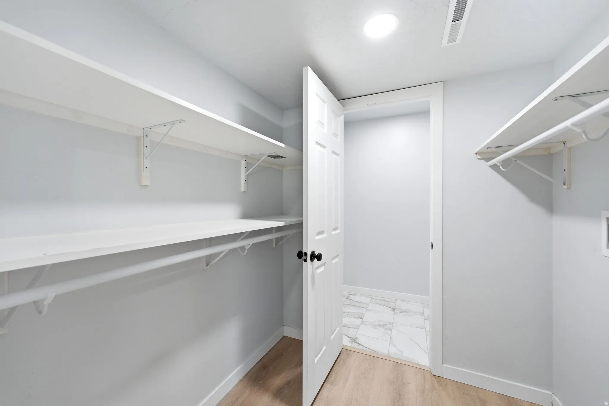 Spacious closet featuring built-in shelving, clothing rods, and wood-finish flooring