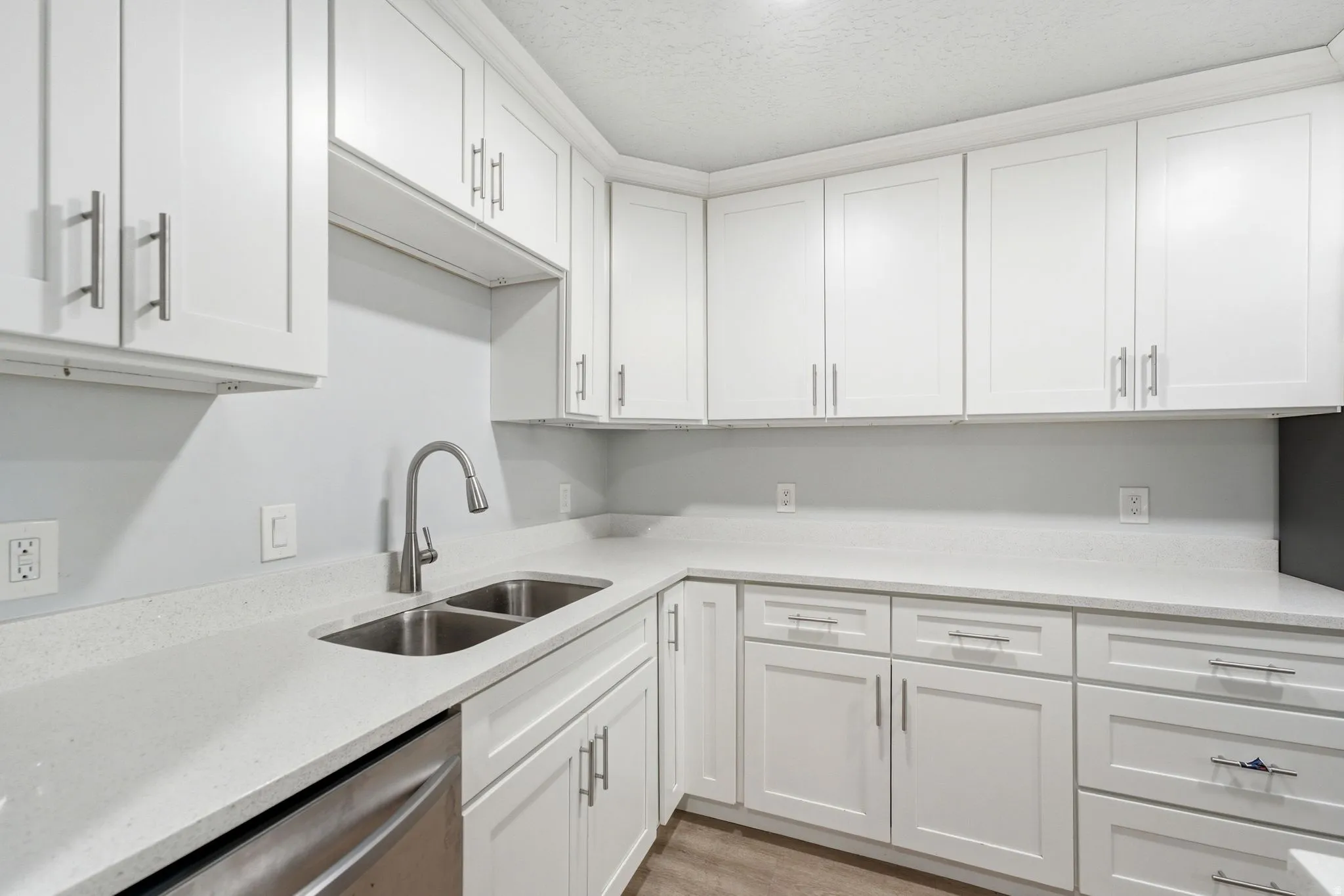 Kitchen featuring white shaker cabinetry, light-toned countertops, a stainless steel double-basin sink, a pull-down faucet, and wood-finish flooring