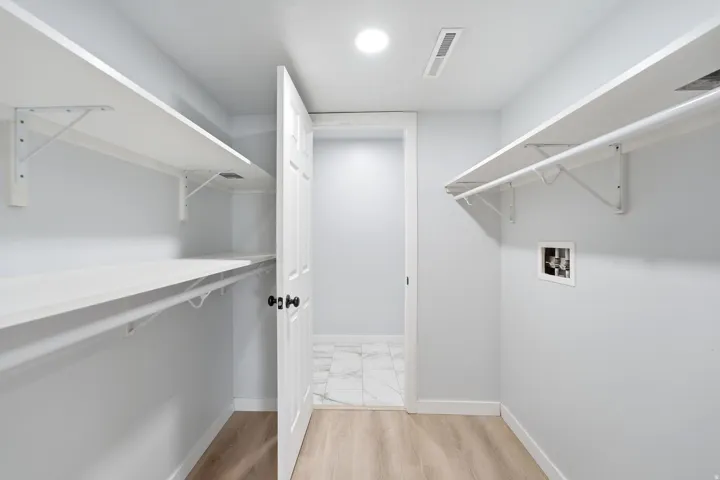 Laundry area featuring wood-finish flooring, white shelving, clothing rods, and a utility hookup
