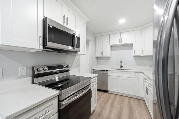 Contemporary kitchen featuring white shaker cabinetry, stainless steel appliances, light-toned countertops, and wood-finish flooring