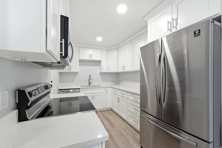 Modern kitchen featuring white shaker cabinetry, stainless steel appliances, quartz countertops, a contemporary sink with a gooseneck faucet, and wood-finish flooring