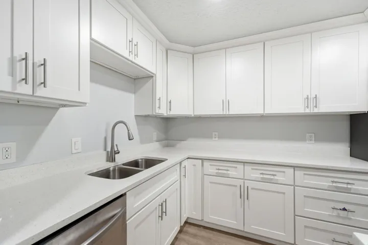 Kitchen featuring white shaker cabinetry, light-toned countertops, a stainless steel double-basin sink, a pull-down faucet, and wood-finish flooring