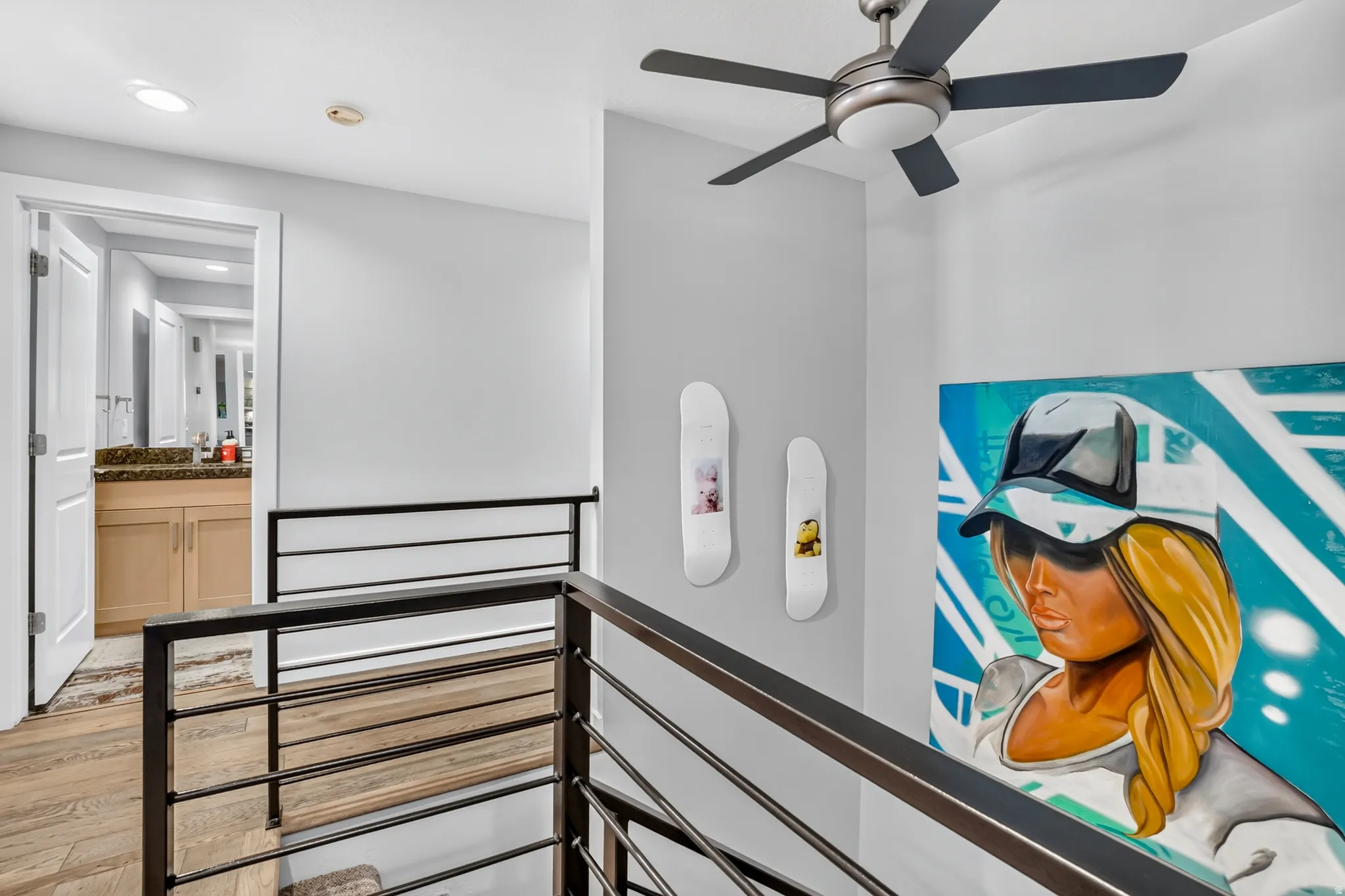Upper-level landing featuring wood-finish flooring, a contemporary ceiling fan, and a view into a bathroom with a dual-sink vanity and stone countertop