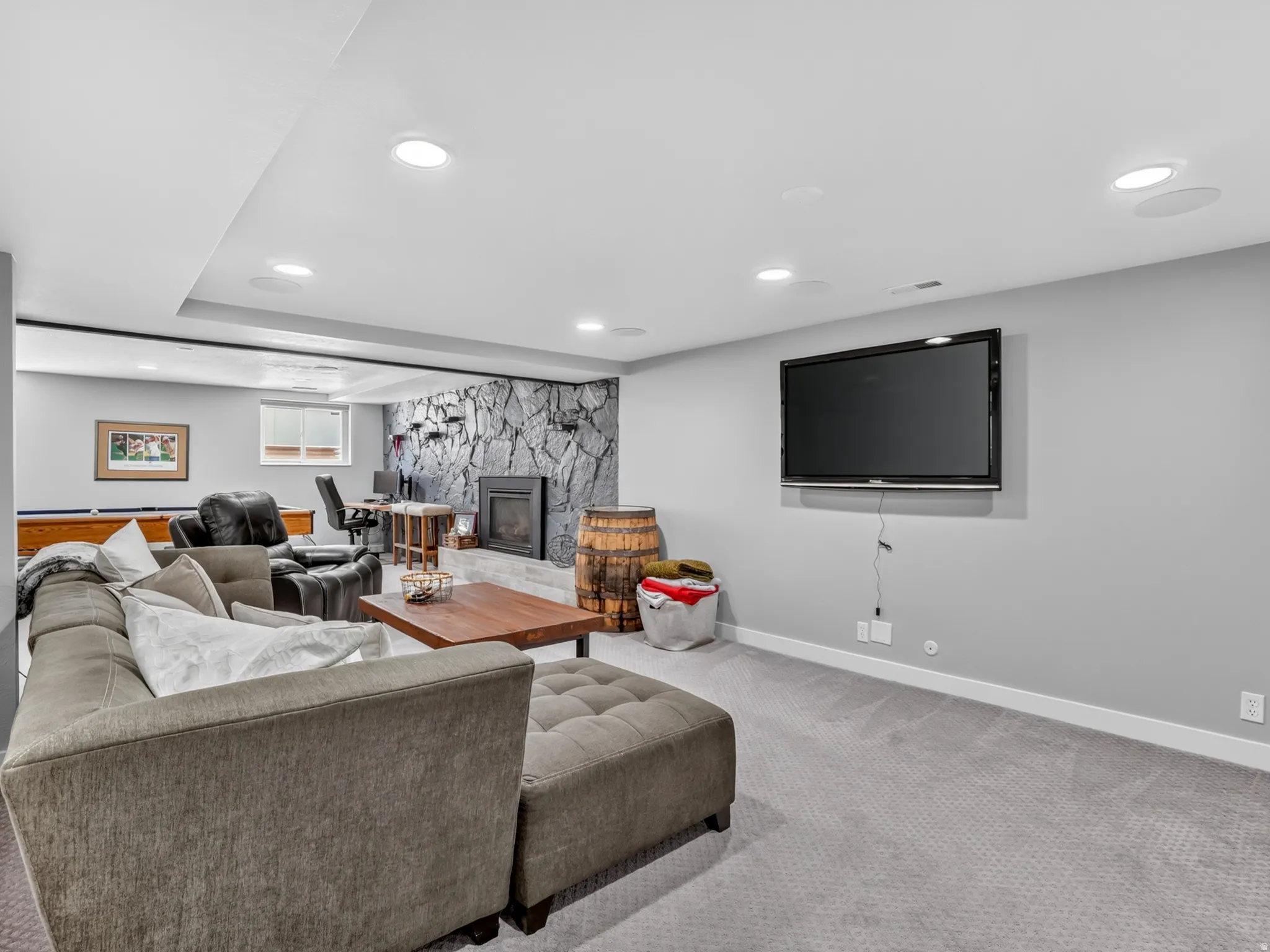 Spacious recreation room featuring recessed lighting, light gray carpet flooring, and a stone accent wall with a built-in fireplace