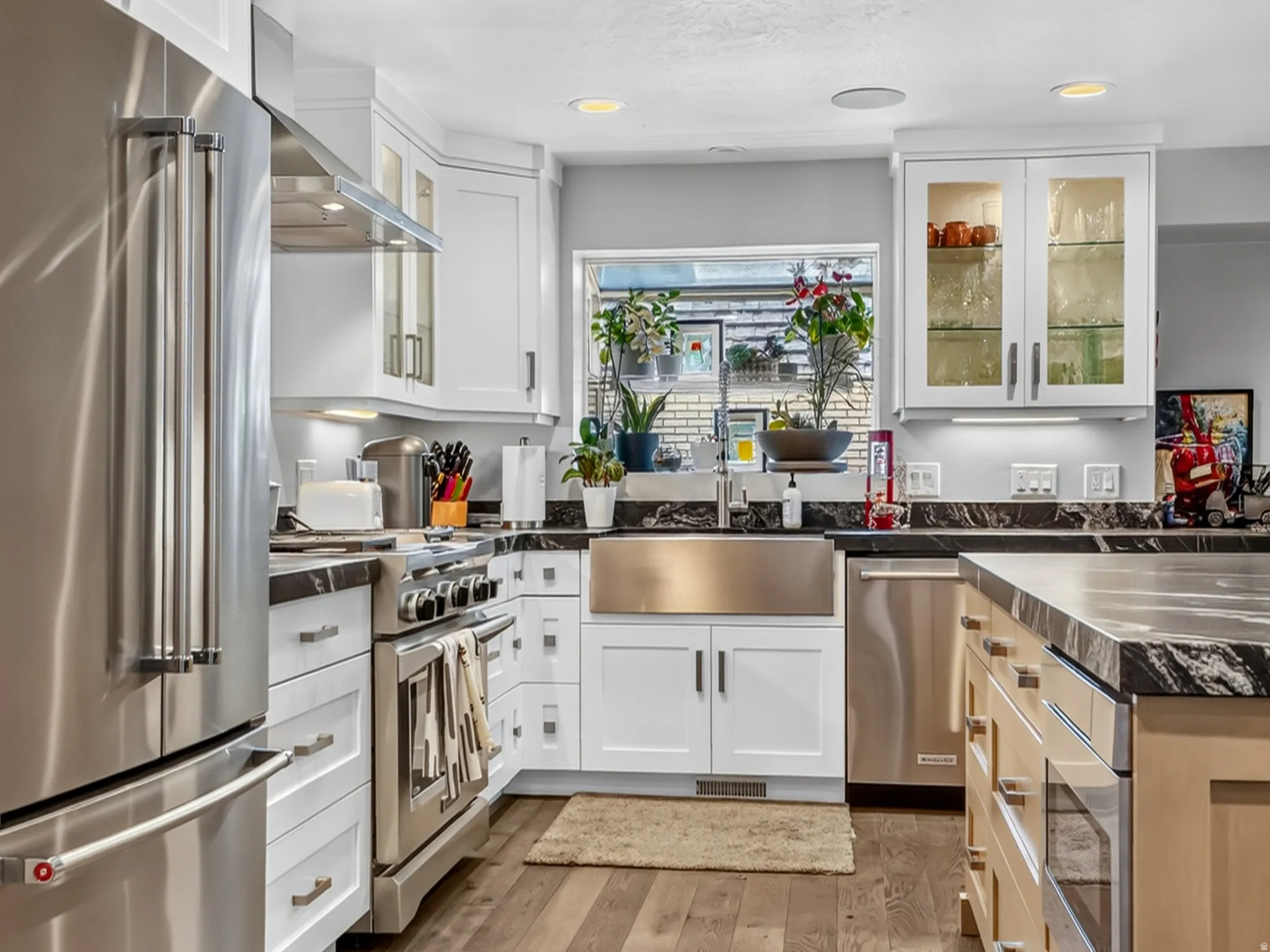 Kitchen featuring wood-finish flooring, white cabinetry, stainless steel appliances, a stainless steel farmhouse sink, and contrasting dark countertops